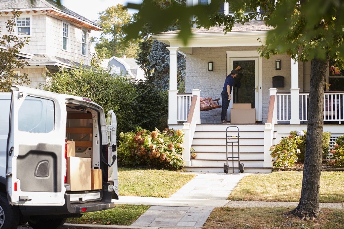 A delivery driver carrying boxes from a van up to a home's front porch in a residential neighborhood